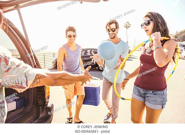 Group of friends standing by car, holding picnic and play items