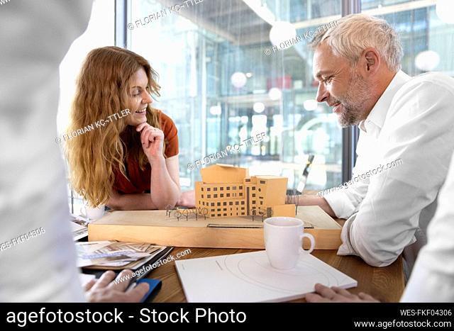 Smiling male and female architect looking at model in office