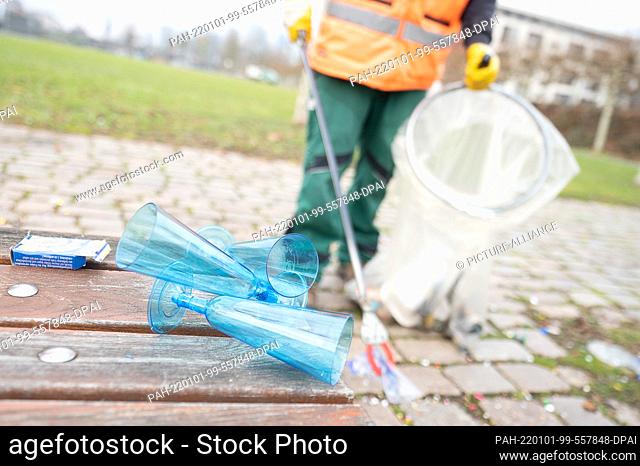 01 January 2022, Hessen, Frankfurt/Main: Champagne glasses lie on the northern bank of the Main River on New Year's Day in front of an employee of a landscaping...
