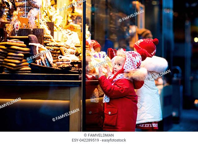 Children window shopping on traditional Christmas market in Germany on snowy winter day. Kids buying candy, pastry and gingerbread in confectionery