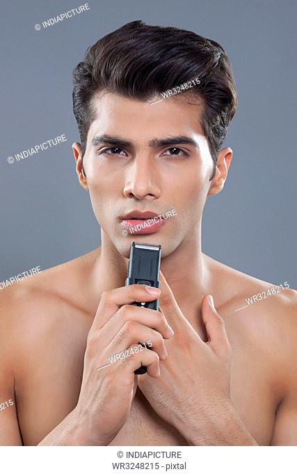 Portrait of young man using electric shaver