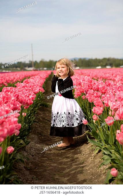 4 year old girl in black and white dress playing and smiling in a tulip fields in Skagit Valley, Washington, USA