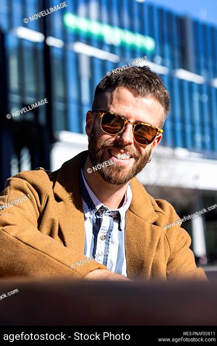 Mid adult businessman smiling while sitting outdoors during sunny day