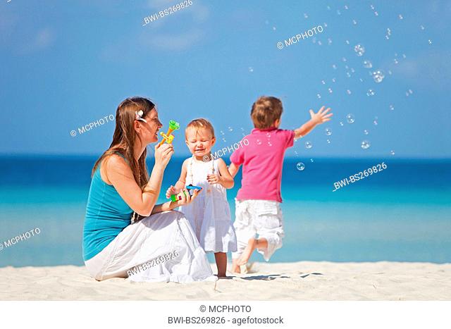 mother sitting with her two children on the beach and blowing bubbles