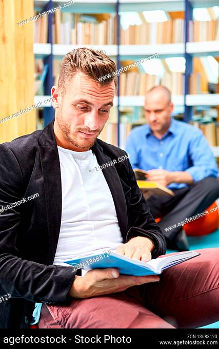 Junger Mann liest konzentriert in einem Buch in der Bibliothek der Volkshochschule