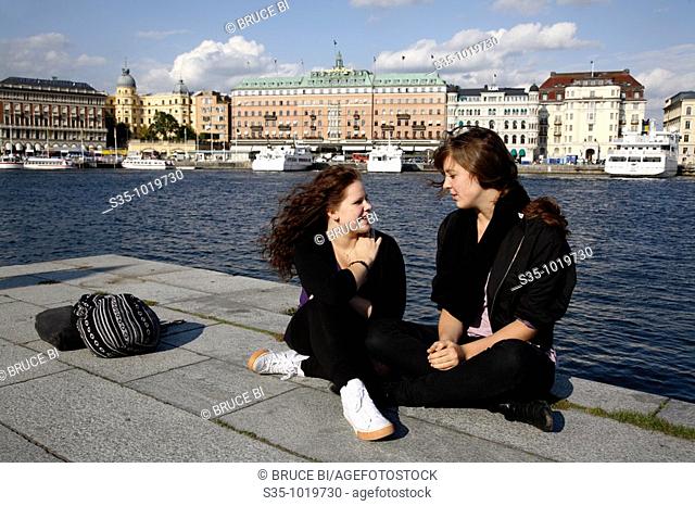 Two local girls relax in the harbor with the 19th century Grand Hotel in the background, Stockholm, Sweden