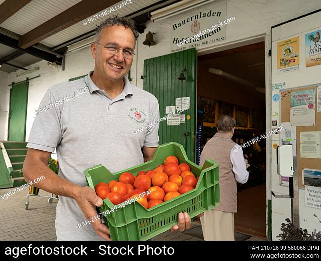 28 July 2021, Hessen, Wiesbaden: Farmer Ralf Schaab from the Erbenheim farm on the outskirts of Wiesbaden stands in front of his farm shop with a crate of...
