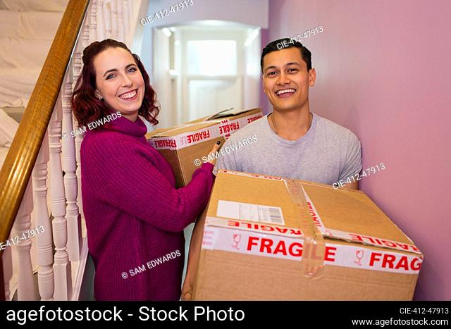Portrait happy couple moving house, carrying cardboard boxes in corridor