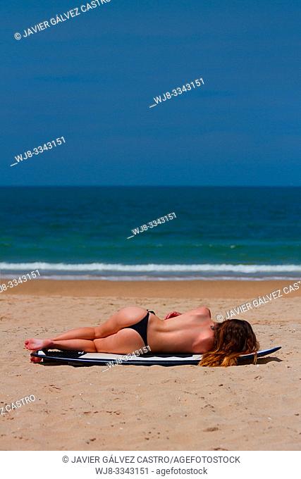 Young woman sunbathing on the beach on her surfboard