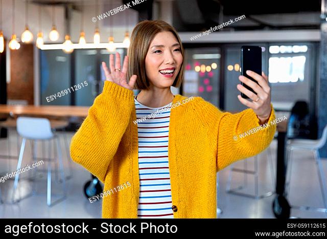 Portrait of asian smiling businesswoman standing having video call using smartphone