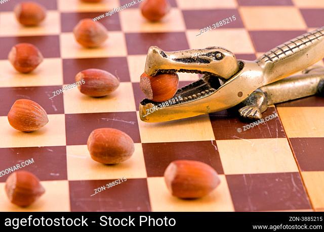 Gold crocodile crush tool with nut in maw on chess board and cobnuts stan like checkers concept