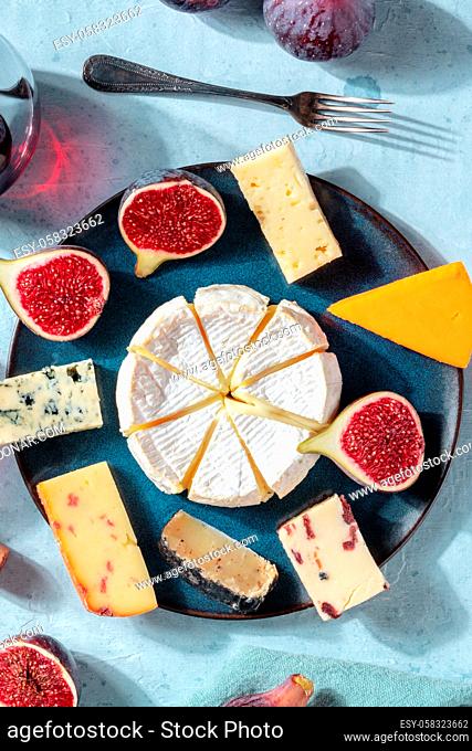 Cheese selection, overhead vertical shot on a plate with fresh figs, on a blue background