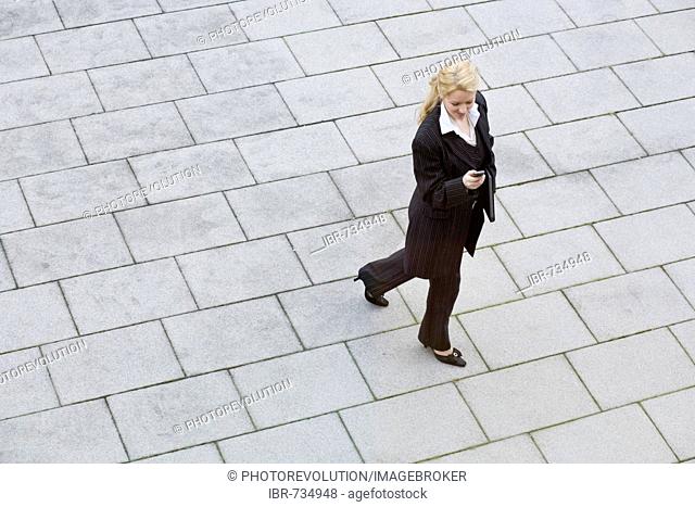 Businesswoman carrying binder under her arm looking at her mobile phone