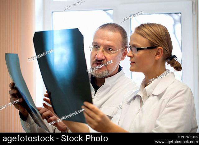Senior and young doctors analyzing and dicussing the result of x-ray examination. They having two images to compare