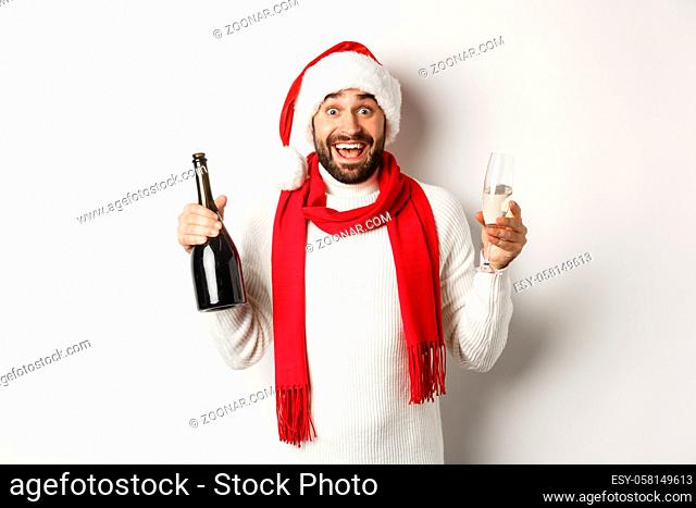 Christmas party and holidays concept. Happy bearded male model in Santa hat and red scarf, celebrating xmas, partying with glass of Champgne, white background