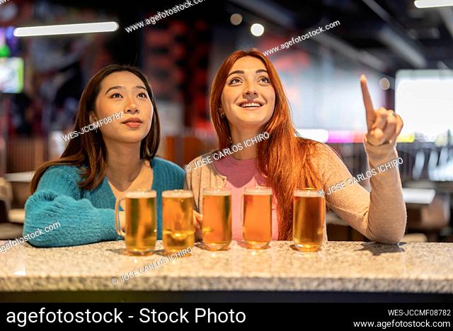 Happy woman pointing to friend with glasses of beer at counter