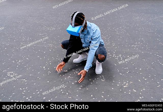 Man wearing virtual reality headset crouching on road