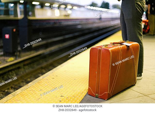 A man with a leather suitcase stands at a train station platform in New York