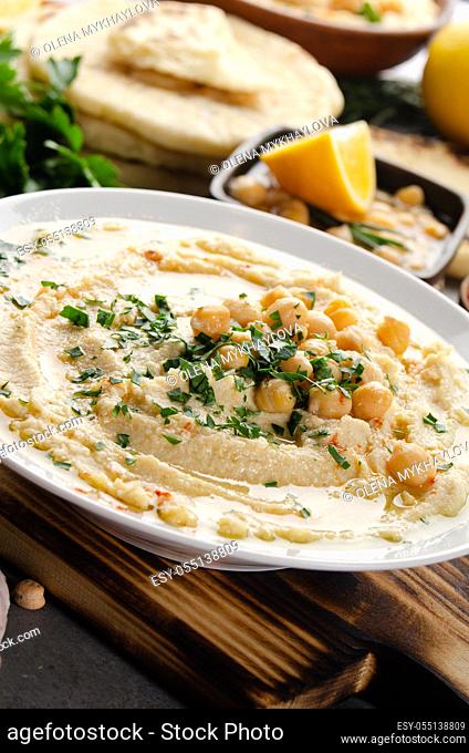 Fresh homemade Hummus in clay dish topped with olive oil, chickpeas and chopped green coriander leaves on stone table served with spices
