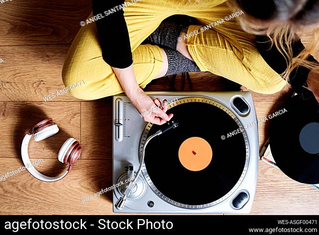 Woman adjusting tonearm of turntable while sitting on floor at home