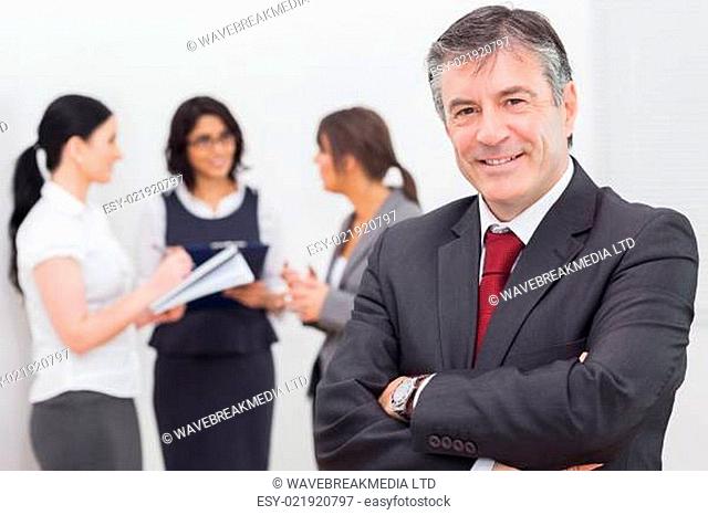 Businessman smiling with arms crossed and three businesswomen speaking