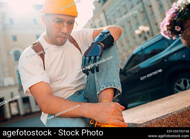 Young disabled sad man with artificial prosthetic hand in casual clothes at city street