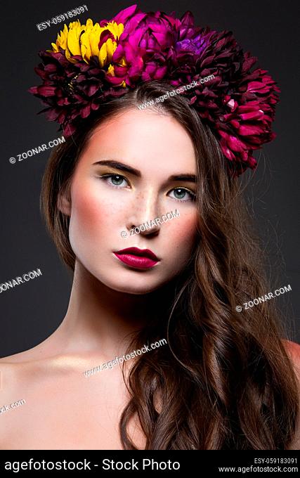 Beautiful young brunette woman with floral head piece in hair over dark background. Beauty shot