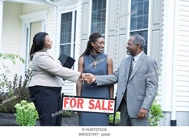Middle-aged man shaking hand with a real estate agent and a middle-aged woman looking at him