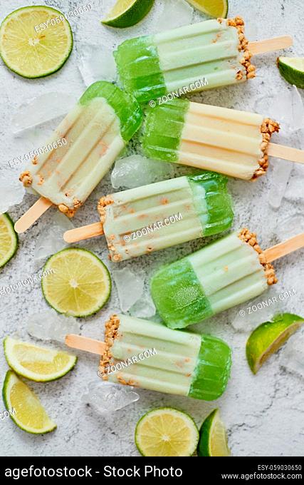 Lime and cream homemade popsicles or ice creams placed with ice cubes on gray stone backdrop. Flat lay, top view