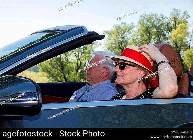 Happy older couple drives with a luxury convertible car on a sunny day