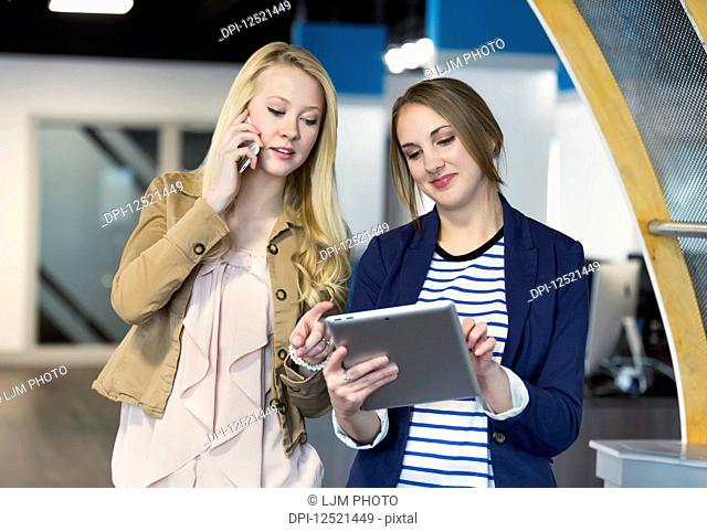 Two beautiful young millennial business women using technology in the workplace; Sherwood Park, Alberta, Canada