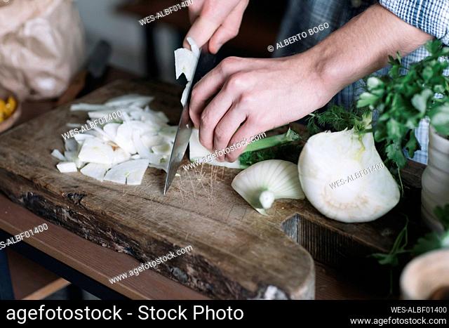 Hands of man cutting fennel on board in kitchen