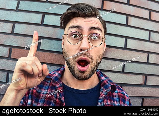 Great idea! Handsome man keeping finger pointed upwards, showing something above his head, making gesture with index finger