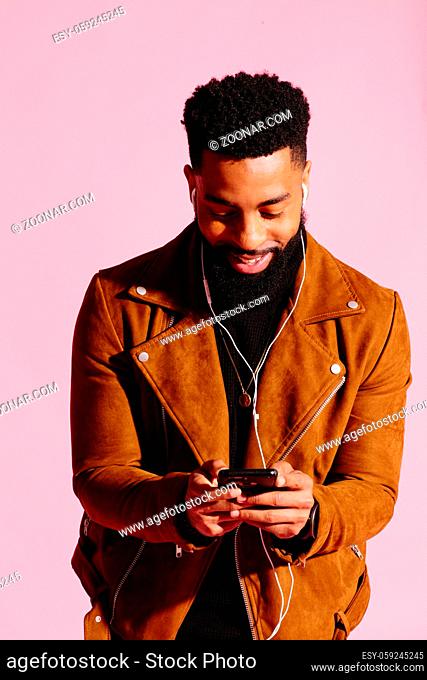 Handsome and cool African American man with beard, listening music, texting, isolated on pink studio background