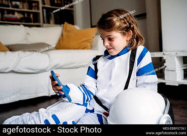 Girl wearing space costume looking at smart phone sitting in living room