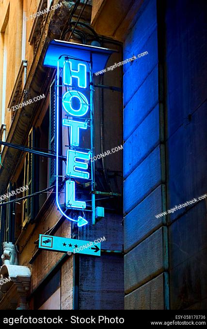 Blue neon hotel sign with arrow on the wall close-up