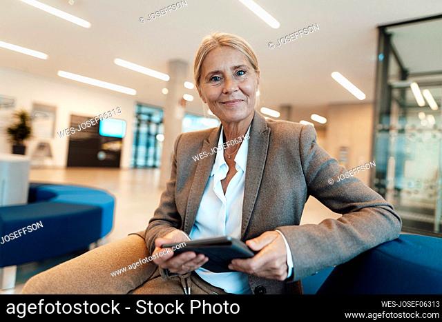 Smiling businesswoman with tablet PC sitting on sofa