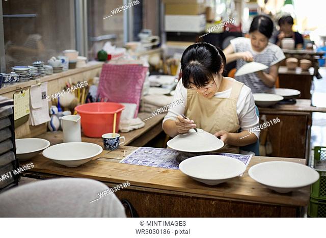 Women sitting in a workshop, working on Japanese porcelain bowls