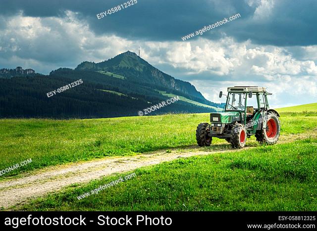 Old tractor on a meadow with fresh grass. Beautiful view to alpine mountains. Alps