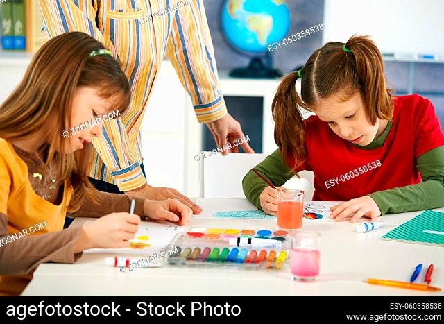 Elementary age children sitting around desk enjoying painting with colors in art class at primary school classroom