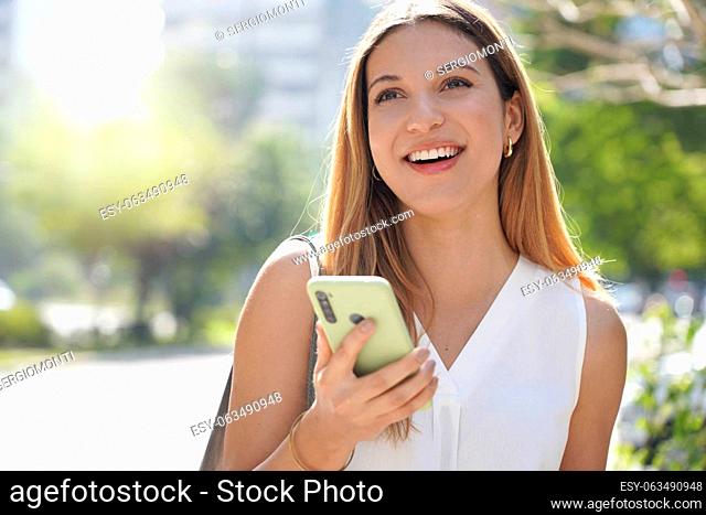 Close-up of laughing casual woman looking away holding her mobile phone outdoors