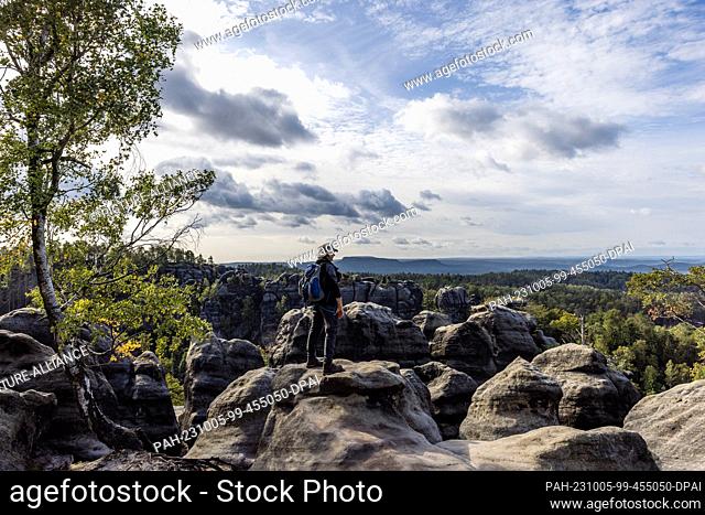 05 October 2023, Saxony, Schmilka: A man stands on the Carolafelsen in the national park ""Saxon Switzerland"" and looks into the distance
