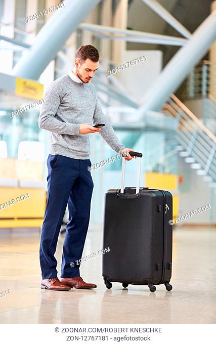 Mann als Passagier mit Gepäck im Flughafen Terminal liest eine SMS auf dem Smartphone