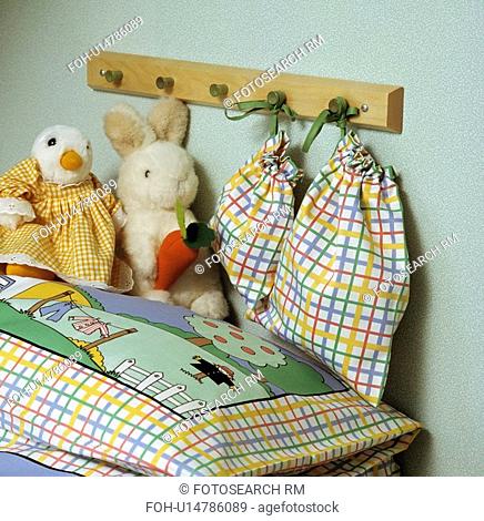 Close up up soft toys on child's pictorial pillow below pegboard with multicoloured checked cotton bags