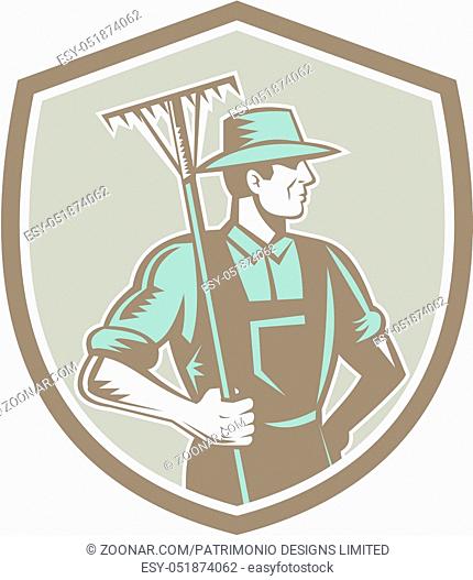 Illustration of organic farmer holding rake on shoulder facing side set inside shield crest on isolated background done in retro woodcut style