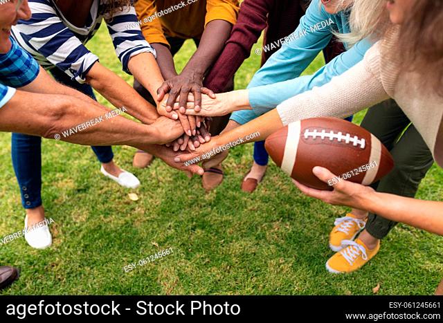 Multiracial senior male and female friends stacking hands while playing rugby in backyard on weekend
