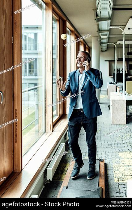 Happy businessman gesturing while talking through mobile phone on treadmill in office