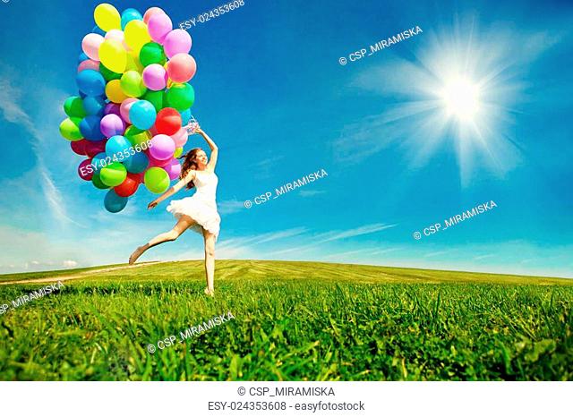 Happy birthday woman against the sky with rainbow-colored air balloons in her hands. sunny and positive energy of nature