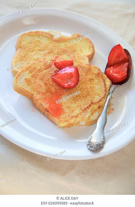 Macerated strawberries spooned over French toast on a white platter