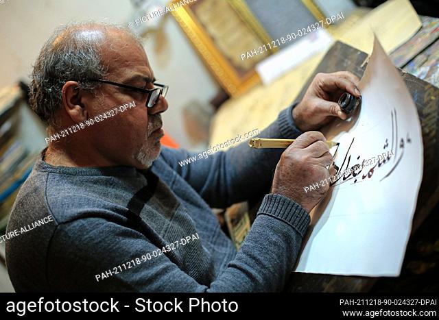 18 December 2021, Iraq, Baghdad: Iraqi Arabic calligraphy master Amin Ragab, 60, uses a reed pen and ink to write versus of poetry at his office in Baghdad on...